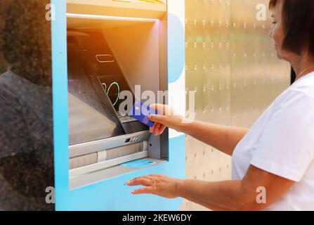 Reife Frau mit Karte von ATM. Frau mit Kreditkarte abheben Geld von Geldautomaten mit NFC kontaktloses WiFi-System. Wireless-Authentifizierung und -Daten Stockfoto