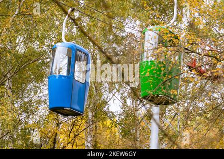 Zwei farbige blaue und grüne Seilbahnkabinen im goldenen Herbstwald. Saisonales Unterhaltungsprogramm Stockfoto