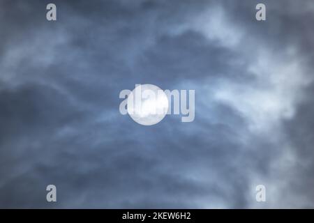 Großer Sonnenkreis, der tagsüber durch Wolken schaut. Sonne in dunkler Wolkenlandschaft Naturphänomen Hintergrund in grauen Farben Stockfoto