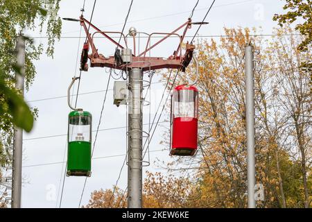 Farbige rote und grüne Seilbahnkabinen im goldenen Kharkiv-Stadtpark im Herbst. Standsäule mit Seilbahnkabinen Stockfoto