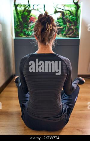 Schöne Frau, die vor dem Aquascape des Aquariums auf dem Boden sitzt. Stockfoto