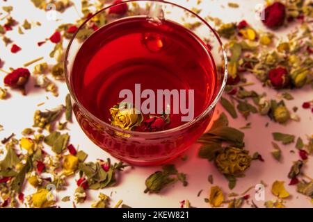 Tee in einer Glasschale mit Rosenknospe auf einem Hintergrund mit Kräuter- und Blumentee Stockfoto