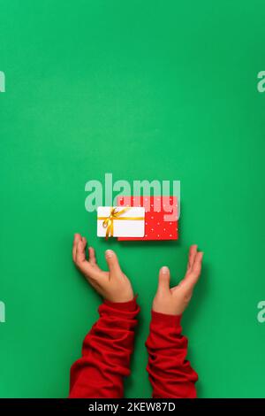 Weibliche Hände halten eine schwebender Bonus- oder Geschenk-Bankkarte und eine Schachtel mit einem Geschenk. Draufsicht, grüner Hintergrund flach liegend Stockfoto