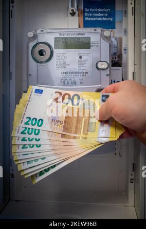 Neben einem elektrischen Zähler ist eine Menge von zweihundert Euro-Banknoten gehalten Stockfoto