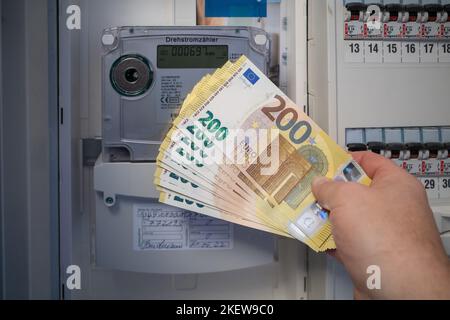 Neben einem elektrischen Zähler ist eine Menge von zweihundert Euro-Banknoten gehalten Stockfoto