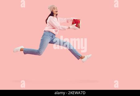 Glücklich aufgeregt Frau hält Neujahr Geschenk, springen und fliegen auf rosa Hintergrund Stockfoto