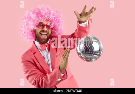 Verrückt fröhlich und lustig Mann spins kleine glänzende Disco-Ball isoliert auf rosa Hintergrund. Stockfoto