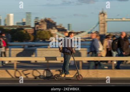 Ein Mann, der während der Hauptverkehrszeit mit einem E-Scooter über die London Bridge fährt. Fahren eines privaten E-Scooters ist illegal, abgesehen von auf Privateigentum in Stockfoto