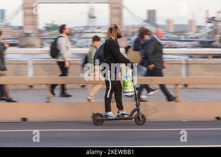 Ein Mann, der während der Hauptverkehrszeit mit einem E-Scooter über die London Bridge fährt. Fahren eines privaten E-Scooters ist illegal, abgesehen von auf Privateigentum in Stockfoto