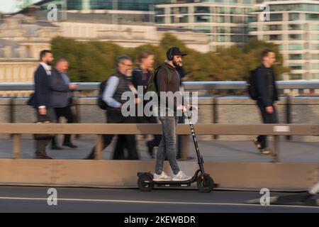 Ein Mann, der während der Hauptverkehrszeit mit einem E-Scooter über die London Bridge fährt. Fahren eines privaten E-Scooters ist illegal, abgesehen von auf Privateigentum in Stockfoto