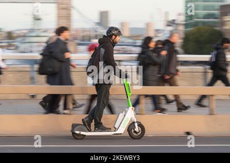 Ein Mann, der während der Hauptverkehrszeit auf einem Lime-E-Scooter fährt, der Teil des „Transport for London“-E-Scooter-Verleihprogramms ist, über die London Bridge. London Bridge, Londo Stockfoto