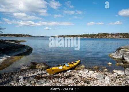 Ein einzelnes Kajak am Ufer einer Insel im Stockholmer Archipel, Schweden. Gelbes Kajak am Strand. Stockfoto