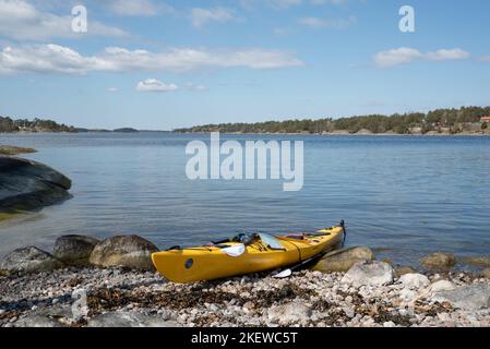 Ein einzelnes Kajak am Ufer einer Insel im Stockholmer Archipel, Schweden. Gelbes Kajak am Strand. Stockfoto