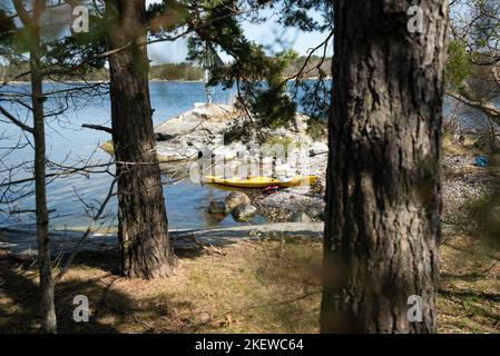 Ein einzelnes Kajak am Ufer einer Insel im Stockholmer Archipel, Schweden. Gelbes Kajak am Strand. Stockfoto