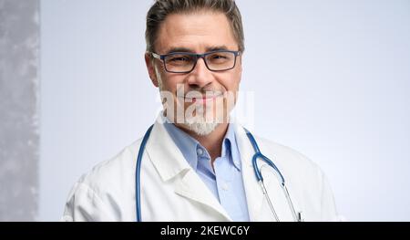 Arzt mittleren Alters in Laborkittel. Freundlicher Arzt, Hausarzt. Mittlerer Erwachsener, Mann im reifen Alter, glücklich lächelnd. Porträt isoliert auf Weiß. Stockfoto