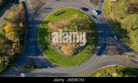 Verkehrskreisel auf einer kleinen Straße, die von Bäumen mit bunten Herbstblättern umgeben ist (Wales, Großbritannien) Stockfoto