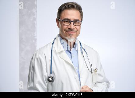 Arzt mittleren Alters in Laborkittel. Freundlicher Arzt, Hausarzt. Mittlerer Erwachsener, Mann im reifen Alter, glücklich lächelnd. Porträt isoliert auf Weiß. Stockfoto