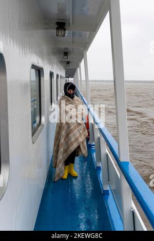 Frau, die in ein Kart gehüllt ist, geht entlang der Seite eines Schiffes, das auf dem Meer segelt Stockfoto