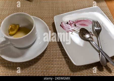 Teller mit Spuren von Lebensmitteln und eine Tasse mit betrunkenem Tee und einem Stück Zitrone Stockfoto