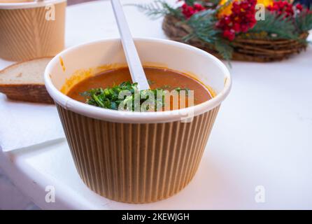 Gulaschsuppe mit Löffel in Papierschüssel. Street-Food-Konzept. Würzige Fleischsuppe. Lifestyle auf der Straße. Reiseküche. Leckeres Abendessen. Leckeres Essen. Stockfoto