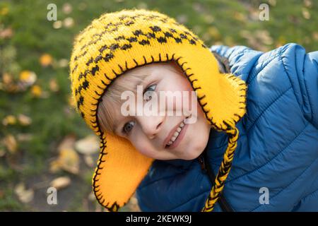 Porträt eines entzückenden Jungen im Vorschulalter mit einem niedlichen Lächeln in einem leuchtend gelben Strickmütze. Gute Laune für einen Spaziergang, positive Einstellung, fröhliche Kindheit. Stockfoto