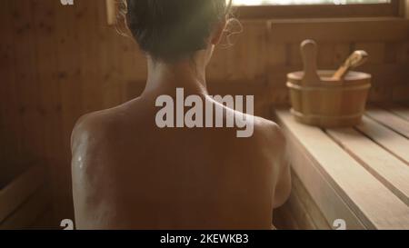 Frau, die sich in der heißen Sauna entspannt und schwitzt. Echter, authentischer Saunamoment. Stockfoto