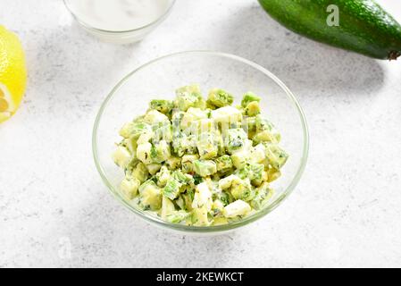 Avocado-Eiersalat in Glasschüssel auf hellem Steingrund. Stockfoto