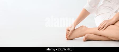 Junge Frau macht Fußmassage auf hellem Hintergrund mit Platz für Text Stockfoto