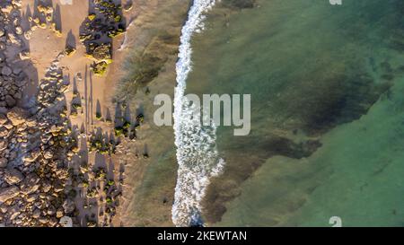 Atemberaubende szenische Drohne Luftaufnahme des Strandes und des Ozeans mit ruhigen Wellen während eines Sonnenuntergangs mit lebendigen Farben. Algarve, Portugal. Klares Wasser. Feiertage Stockfoto