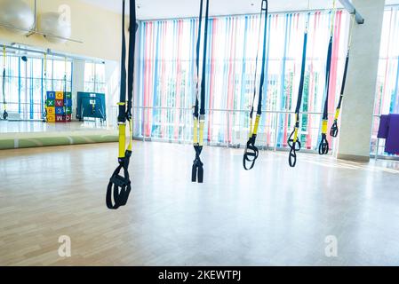 TRX Fitnessbänder für das Arbeiten mit eigenem Gewicht. TRX-Fitnessgurte hängen im leeren Fitnessstudio Stockfoto