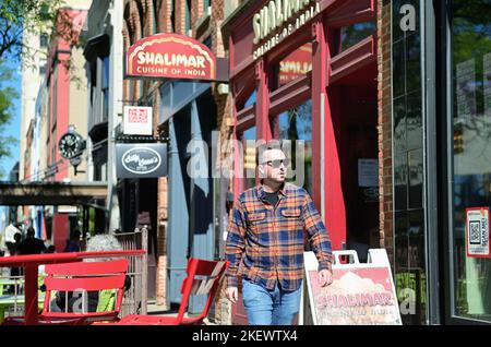 Ann Arbor, Michigan, USA. Mann, der in der Nähe des Campus der University of Michigan eine Straße mit Geschäften, Restaurants und Geschäften entlang läuft. Stockfoto