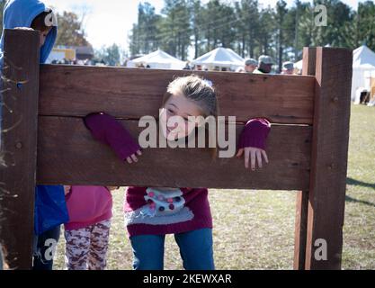 Kershaw, South Carolina, USA. 13.. November 2022. Fans des Revolutionären Krieges und leidenschaftliche Schauspieler stellen die Schlacht von Camden, SC, nach, sodass Besucher während des Krieges um die Unabhängigkeit von der britischen Herrschaft lebendige Geschichte erleben können. Die Schlacht von Camden, die 1780 ausgetragen wurde, war eine von mehreren verheerenden Niederlagen, die die Amerikaner in den frühen Phasen der britischen Militäroffensive im Süden erlitten haben. Im Bild: Ein junges Mädchen wird an einem Pranger gehalten, einem Gerät mit Löchern zur Sicherung von Kopf und Händen von Personen, die unter anderem wegen Trunkenheit oder Pferdediebstahl angeklagt sind. Früher für punis verwendet Stockfoto