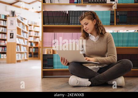 Teenager-Mädchen mit einem Notizbuch in den Händen. Sie ist von Bücherstapeln umgeben. Tag Buchen. Stockfoto