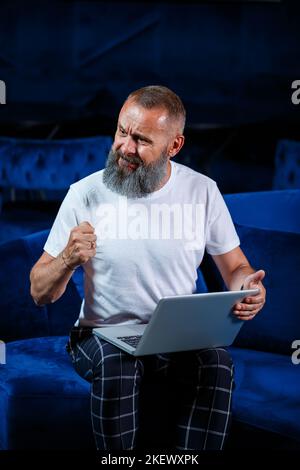 Der männliche Geschäftsmann sitzt mit einer Tasse Kaffee und macht ein neues Projekt mit Grimassen im Gesicht. Stockfoto