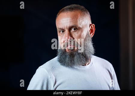 Emotionales Porträt eines erwachsenen grauhaarigen Mannes mit Bart In einem weißen T-Shirt Stockfoto