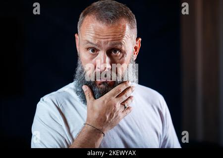 Emotionales Porträt eines erwachsenen grauhaarigen Mannes mit Bart In einem weißen T-Shirt Stockfoto