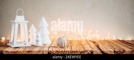 Weiße Weihnachtsbäume, Kerzenlaterne und Bokeh-Lichter auf einem Holztisch in gemütlicher Atmosphäre Stockfoto