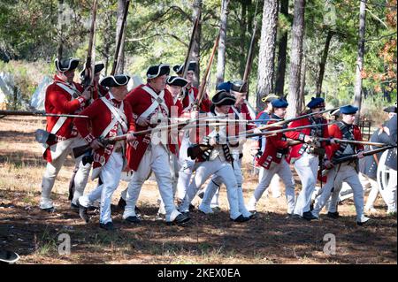 Kershaw, South Carolina, USA. 13.. November 2022. Fans des Revolutionären Krieges und leidenschaftliche Schauspieler stellen die Schlacht von Camden, SC, nach, sodass Besucher während des Krieges um die Unabhängigkeit von der britischen Herrschaft lebendige Geschichte erleben können. Die Schlacht von Camden, die 1780 ausgetragen wurde, war eine von mehreren verheerenden Niederlagen, die die Amerikaner in den frühen Phasen der britischen Militäroffensive im Süden erlitten haben. Im Bild: Britische Soldaten marschieren mit befestigten Bajonetten durch den Wald, um dort den kolonialen Truppen zu begegnen. (Bild: © Robin Rayne/ZUMA Press Wire) Stockfoto