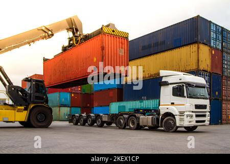 LKW während der Verladung in logistischer Werft mit Frachtcontainer. Gabelstapler, der mit dem Stapler gefahren wird. Logistisches Exportkonzept für den Import. Laden und Entladen Stockfoto