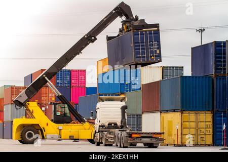 LKW während der Verladung in logistischer Werft mit Frachtcontainer. Gabelstapler, der mit dem Stapler gefahren wird. Logistisches Exportkonzept für den Import. Laden und Entladen Stockfoto