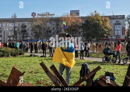 CHERSON, UKRAINE - 14. NOVEMBER 2022 - Ein Mann mit der ukrainischen Flagge und dem Tryzub steht hinter Panzerabwehrhindernissen (tschechischen Igeln) im Zentrum von Cherson, befreit von russischen Invasoren, der Südukraine. Stockfoto