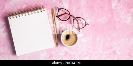 Arbeiten Sie von zu Hause aus. Schreibtisch mit leerem Notizblock, Kaffeetasse, Stift, Brille auf rosafarbenem Tisch. Flach, oben liegend, Kopieplatz Stockfoto