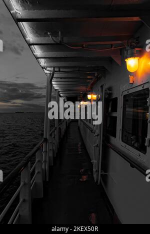 Bunte Lichter bei der abendlichen Bootstour auf dem Meer. Schwarz-weiße Postkarte von einem Kreuzfahrtschiff. Bunte Lichter in einem Schwarzweißfoto. Stockfoto