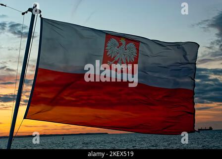 Polnische Flagge im Wind, polnische Seefahne, polnische Seefahne, Hintergrund des Abendhimmels. Die derzeit gültige Flagge in der Zivilschifffahrt. Stockfoto