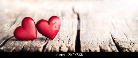 Zwei Rote Hand Geschnitzte Holzherzen Auf Rustikalem Tisch Mit Sonnenlicht Und Bokeh - Valentinstag Stockfoto