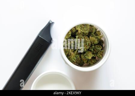 Cannabis flos, medizinisches Marihuana in weißem Behälter neben Verdampfer, sichere Art und Weise, Medizin zu nehmen Stockfoto