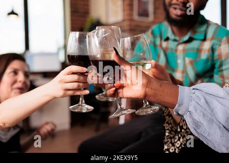 Menschen aus mehreren ethnischen Gruppen Hände Nahaufnahme Schuss Toasting, klirrrende Weingläser auf Wohnung Party. Verschiedene Nationalitäten Freunde feiern, genießen zusammen bei der Hausversammlung. Stockfoto