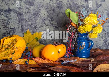 Herbstkomposition. Herbstkomposition bestehend aus Chrysanthemen, Kürbissen, Herbstblättern und Kastanien, Kaki. Stockfoto