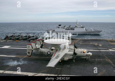Ein E-2D Hawkeye, der an die „Bärenasse“ der Airborne Command and Control Squadron 124 angeschlossen ist, landet auf dem erstklassigen Flugzeugträger USS Gerald R. Ford (CVN 78), als Seeleute an Bord der niederländischen Fregatte HNLMS De Zeven Provincien (F 802) den Flugbetrieb von Ford beobachten, 12. November 2022. Übung Silent Wolverine ist eine von den USA geführte kombinierte Trainingsübung, bei der die Fähigkeiten von Flugzeugträgern der Ford-Klasse durch integrierte High-End-Marinekriegsszenarien sowie teilnehmende Verbündete im Ostatlantischen Ozean getestet werden. Die Gerald R. Ford Carrier Strike Group wird im Atlantischen Ozean eingesetzt und leitet Stockfoto