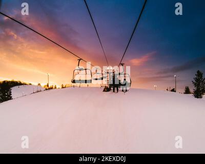 Wunderschöner farbenprächtiger Sonnenuntergang, während die Skifahrer mit dem Lift auf den Berg fahren Stockfoto